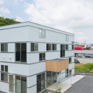 六層二階建ての窓/リナスト障がい者福祉施設 北東側昼景　奥に赤い電車が見える